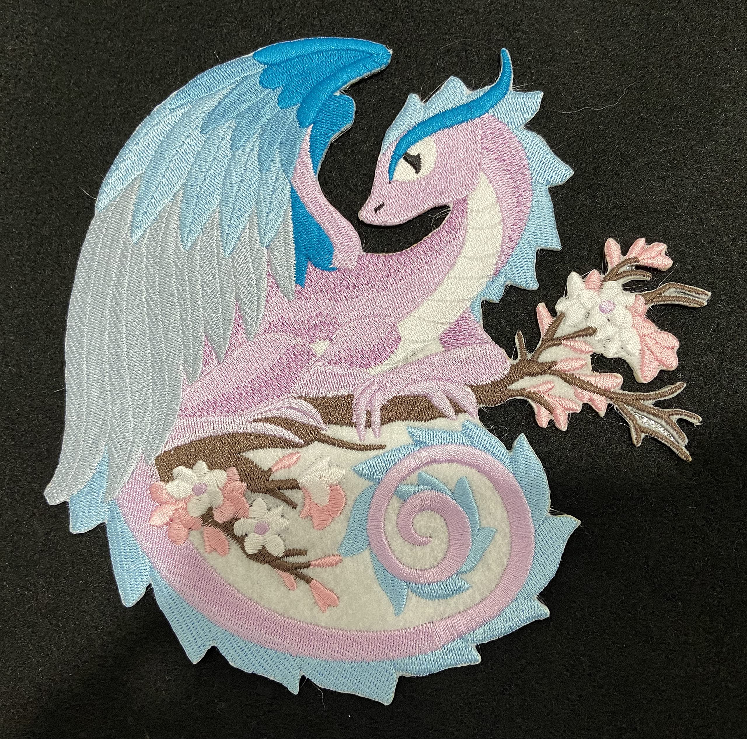 Embroidered patch of a dragon with floral elements on a black background