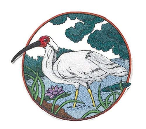 Embroidered patch of a white bird with a red head in a natural setting.